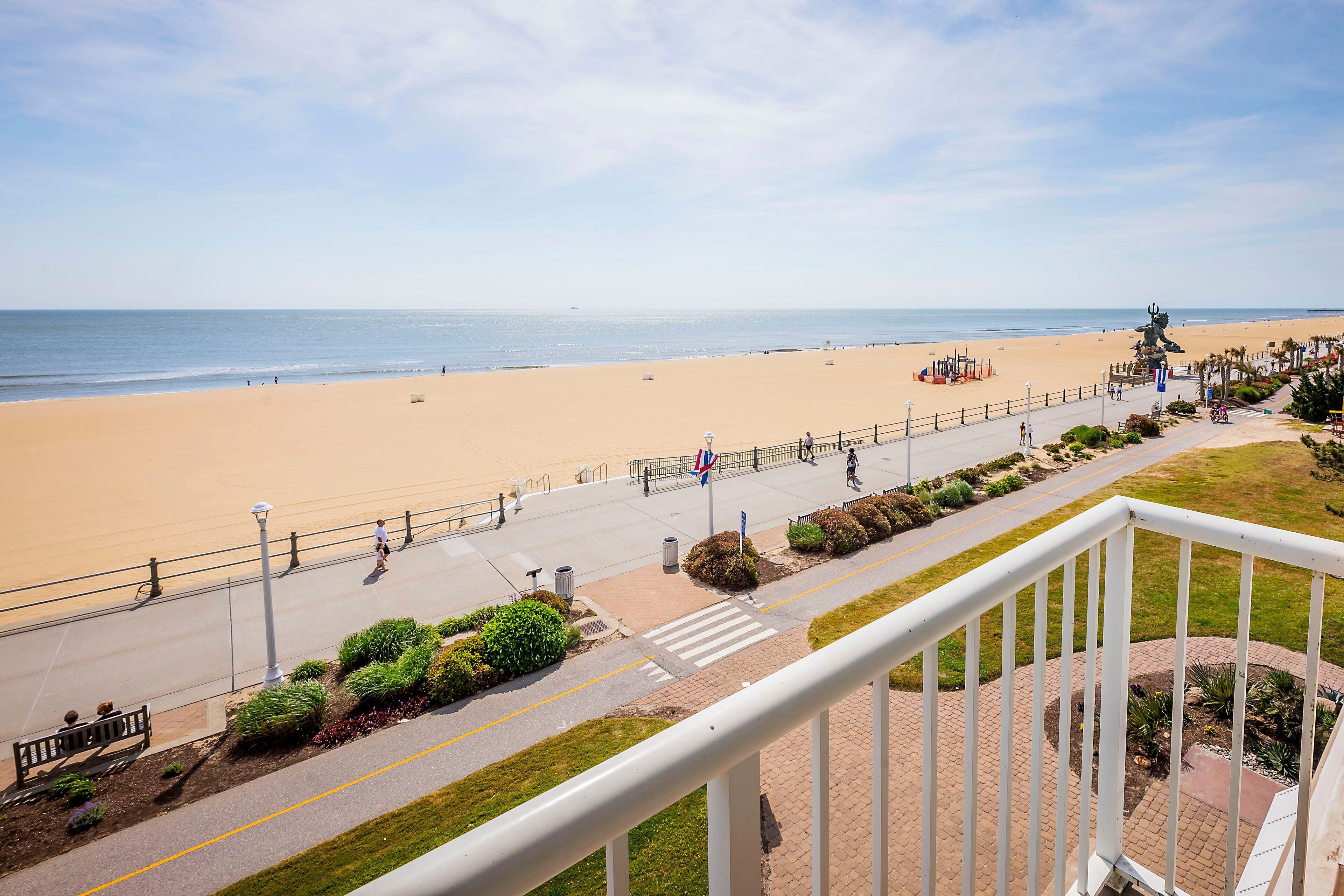 A beach view from a balcony with a railing, a pedestrian path, and a statue.
