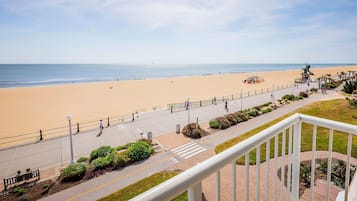 A beach view from a balcony with a railing, a pedestrian path, and a statue.