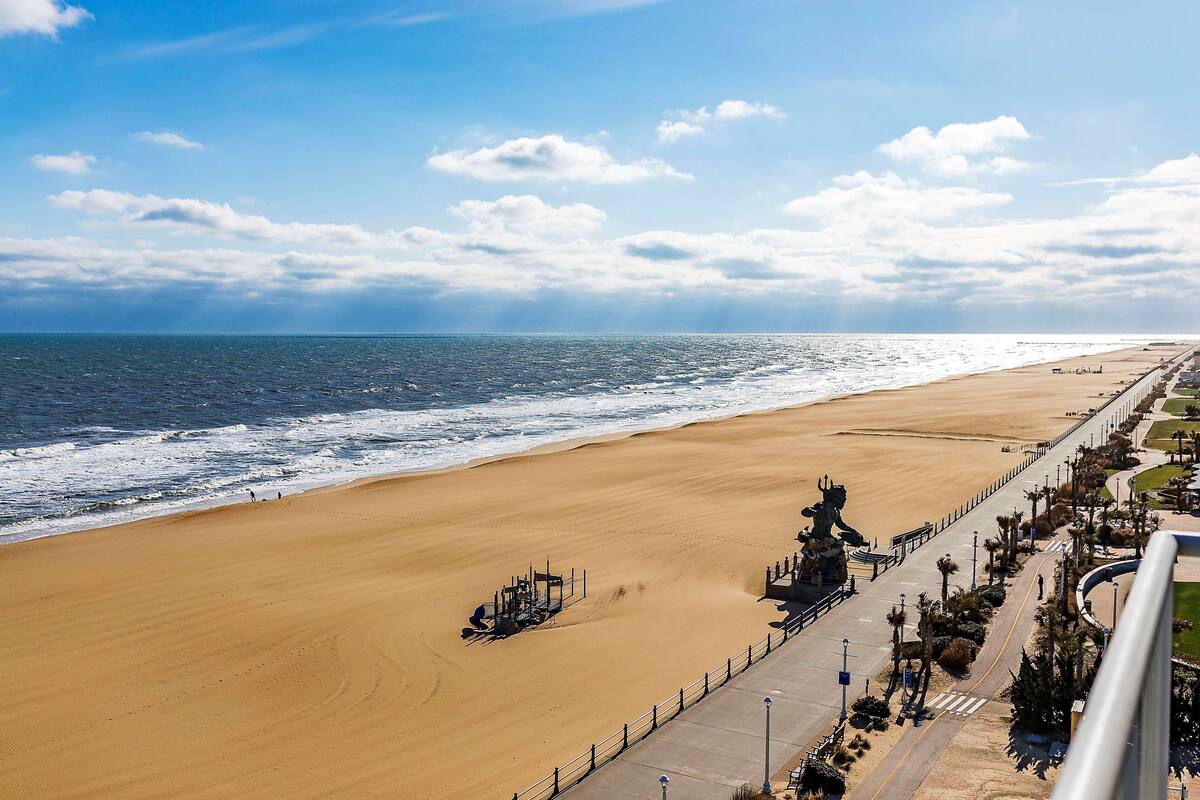 A beach with a paved walkway, a statue, and a clear view of the ocean.