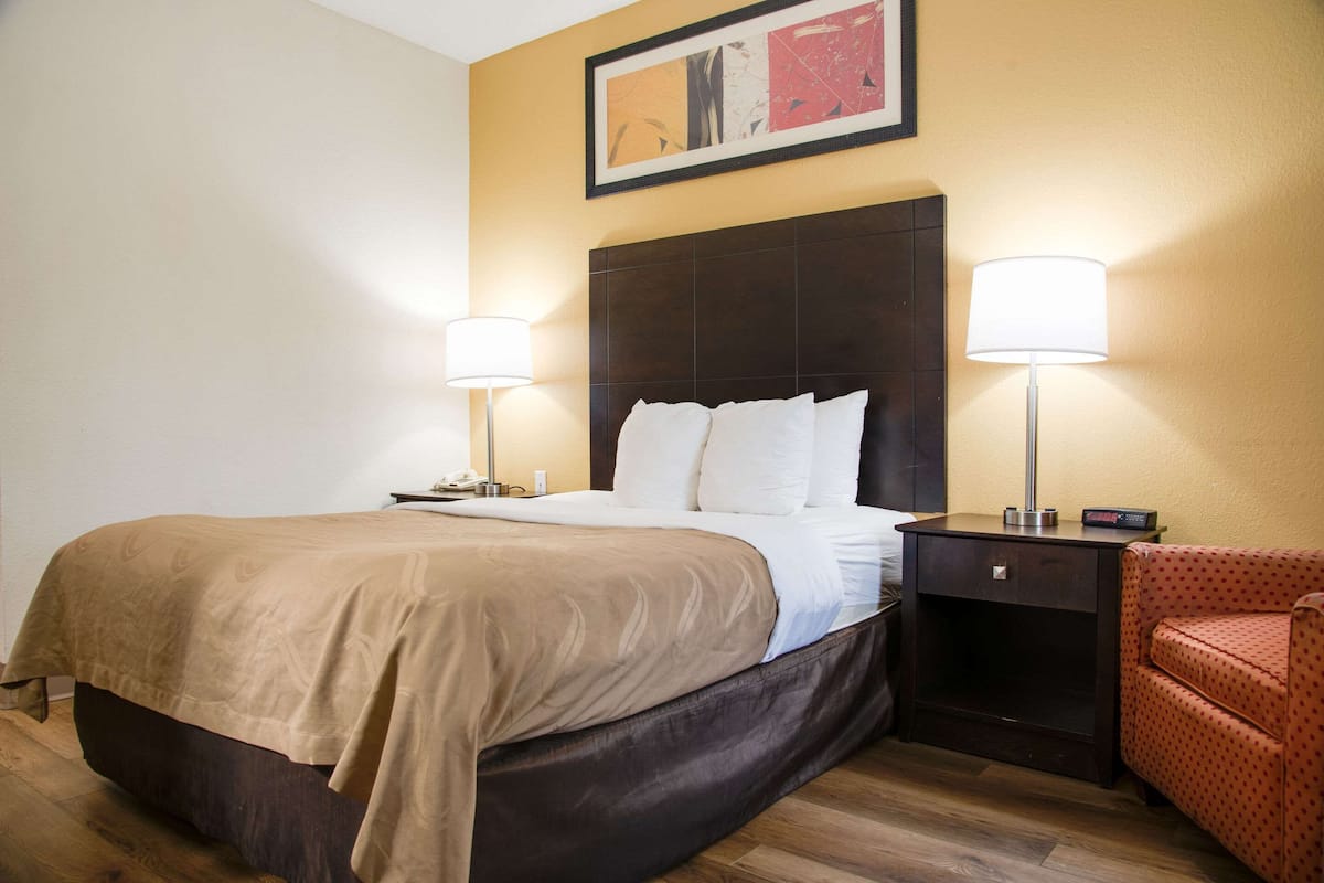 A hotel room with a large bed, two bedside lamps, a nightstand, and a red chair.
