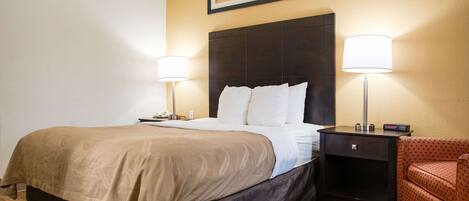 A hotel room with a large bed, two bedside lamps, a nightstand, and a red chair.