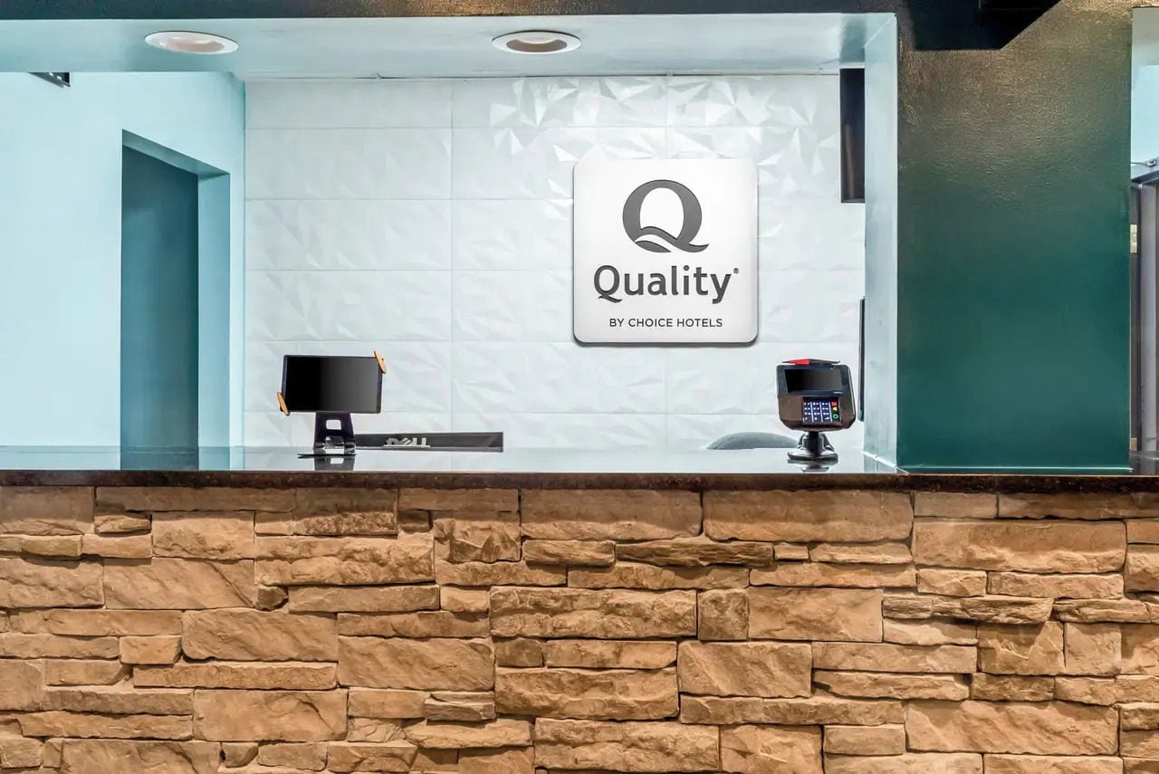 Un comptoir d’accueil avec une enseigne « Qualité par Choice Hotels », un écran d’ordinateur et un terminal de paiement.