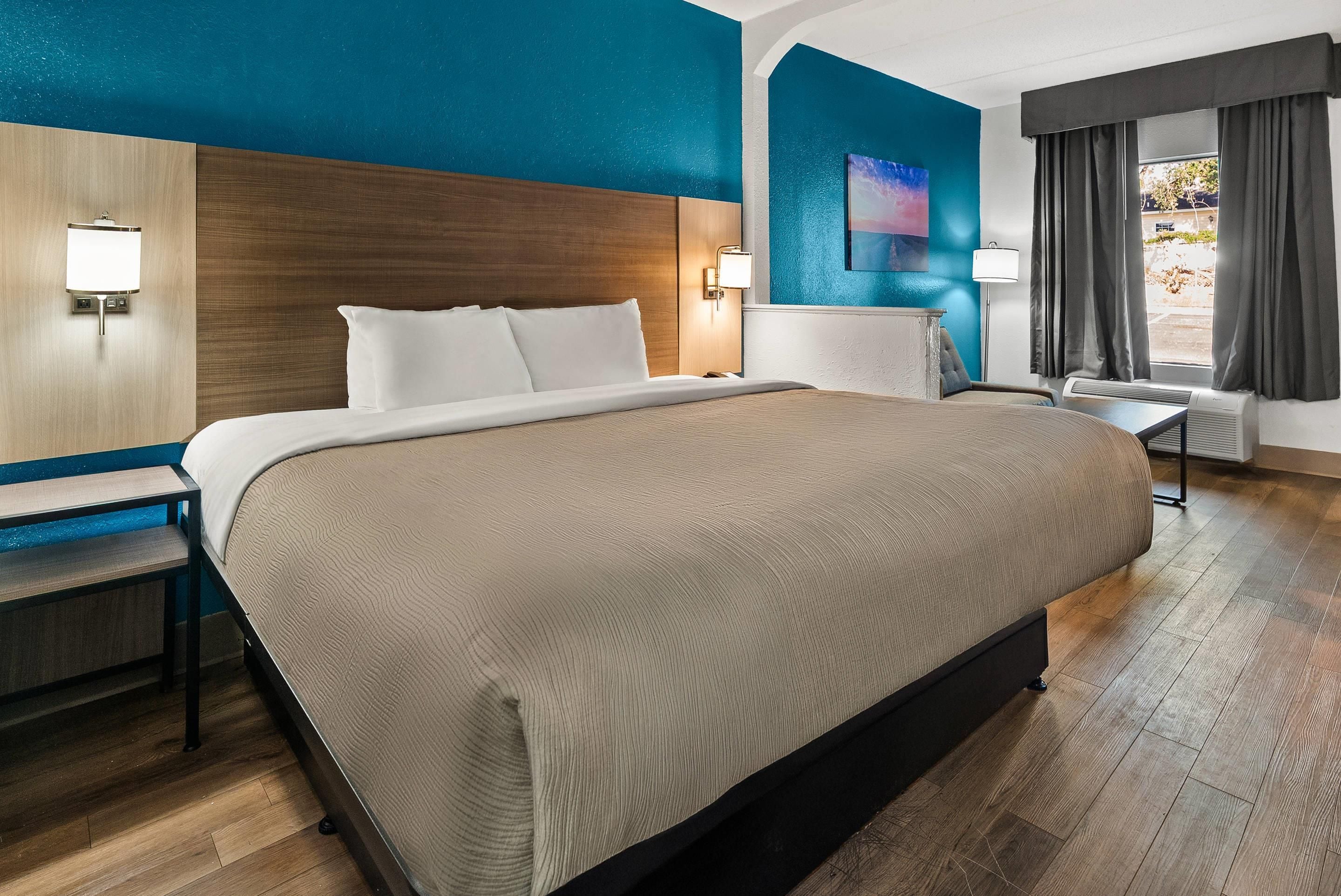 Ein Hotelzimmer mit einem großen Bett, einem Schreibtisch, einem Sessel, einer Lampe und einem Gemälde an der Wand.