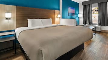 Ein Hotelzimmer mit einem großen Bett, einem Schreibtisch, einem Sessel, einer Lampe und einem Gemälde an der Wand.