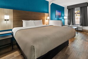 Una habitación de hotel con una cama grande, un escritorio, una silla, una lámpara y un cuadro en la pared.