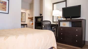 Een hotelkamer met een bed, een bureau met een computer, een stoel, een dressoir en een televisie.