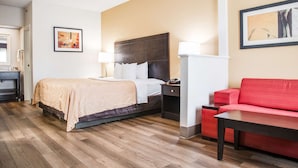 A hotel room with a bed, bedside table, lamp, and a red sofa.