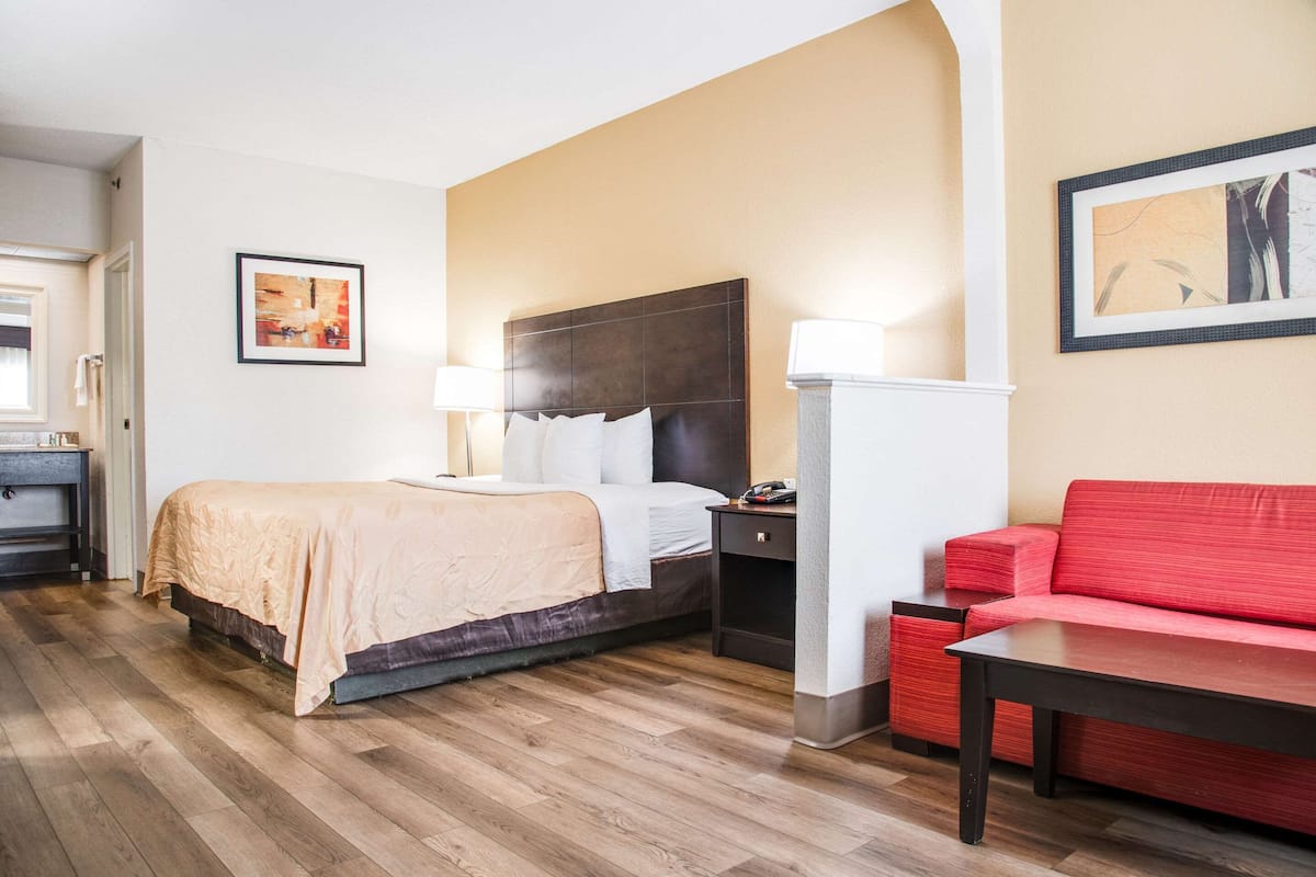 A hotel room with a bed, bedside table, lamp, and a red sofa.