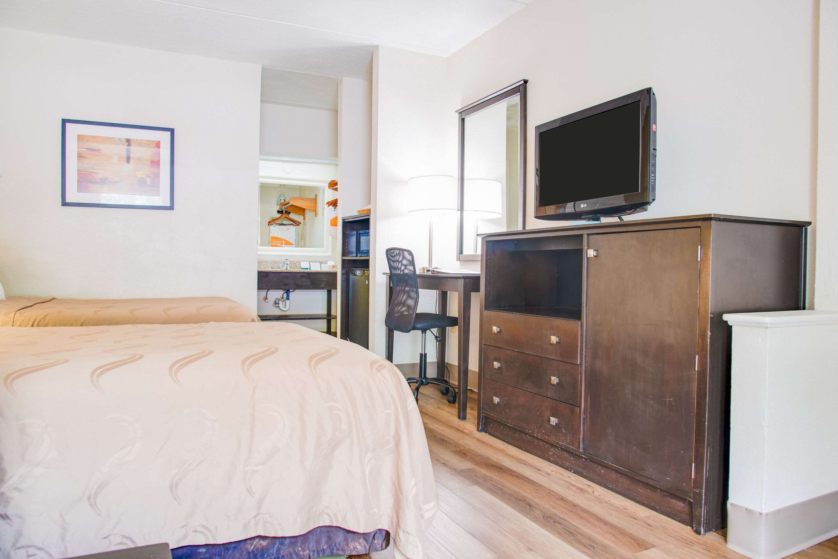 Una habitación de hotel con una cama, un escritorio con computadora, un televisor y un armario.