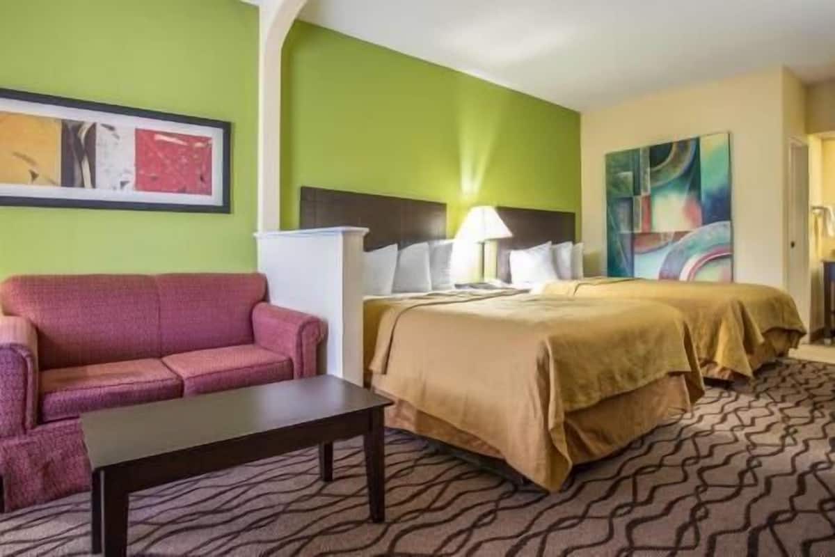 A hotel room with a bed, a sofa, a table, and a painting on the wall.
