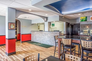 A hotel lobby with a reception desk, a bar area, and a seating area with chairs and tables.