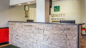 A reception desk with a stone facade, a sign reading "Quality Inn & Suites," and a logo above the sign.