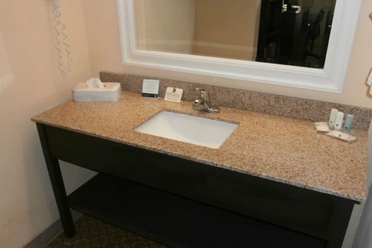 A bathroom with a granite countertop, a white sink, a mirror, a towel dispenser, and a soap dispenser.
