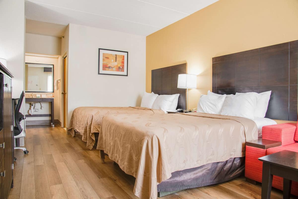 A hotel room with a large bed, a desk with a chair, a mirror, and a red sofa.