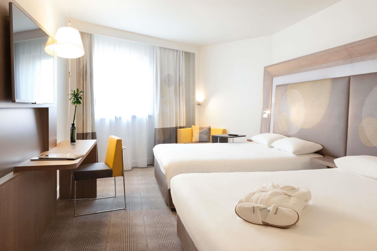 A hotel room with two beds, a desk, a chair, a TV, and a window with curtains.