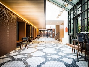 A corridor with patterned flooring, seating areas, and large windows. - Novotel Paris Les Halles (Paris)