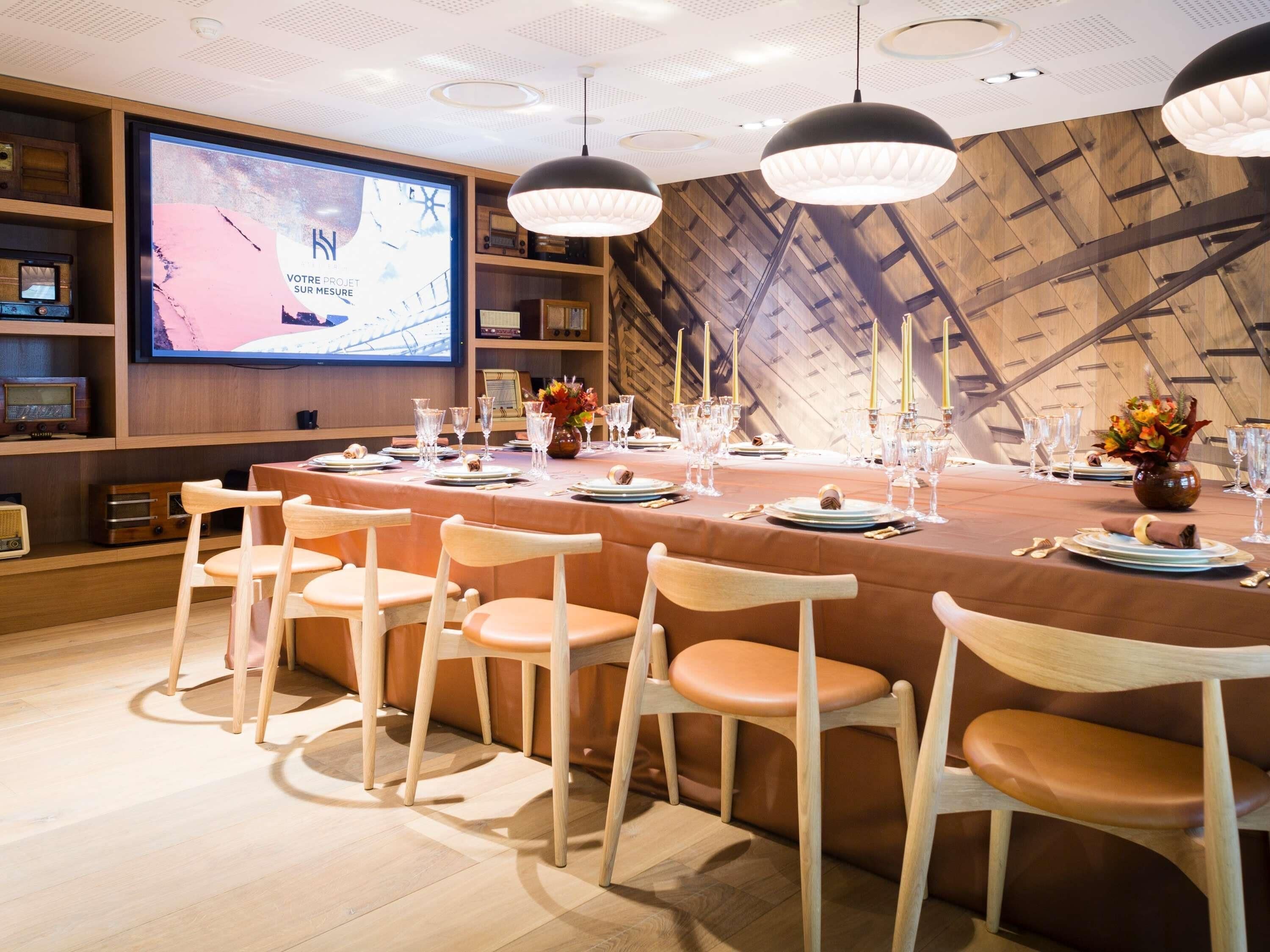 A conference room with a long table set for a meeting, wooden chairs, a large screen, and pendant lighting.