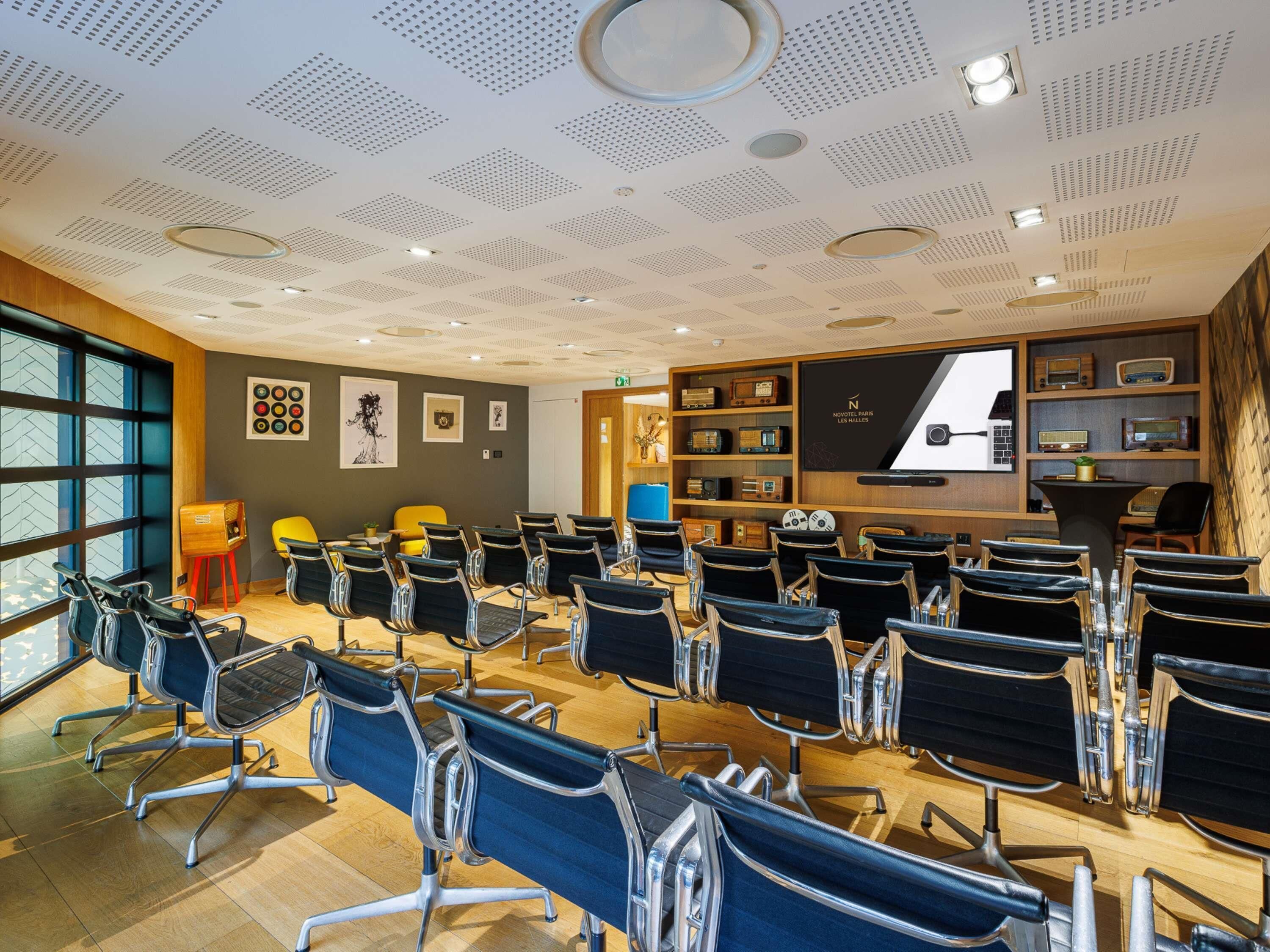 Ein Konferenzraum mit Stuhlreihen, einer Projektionsleinwand und einer Wand mit alten Radios.