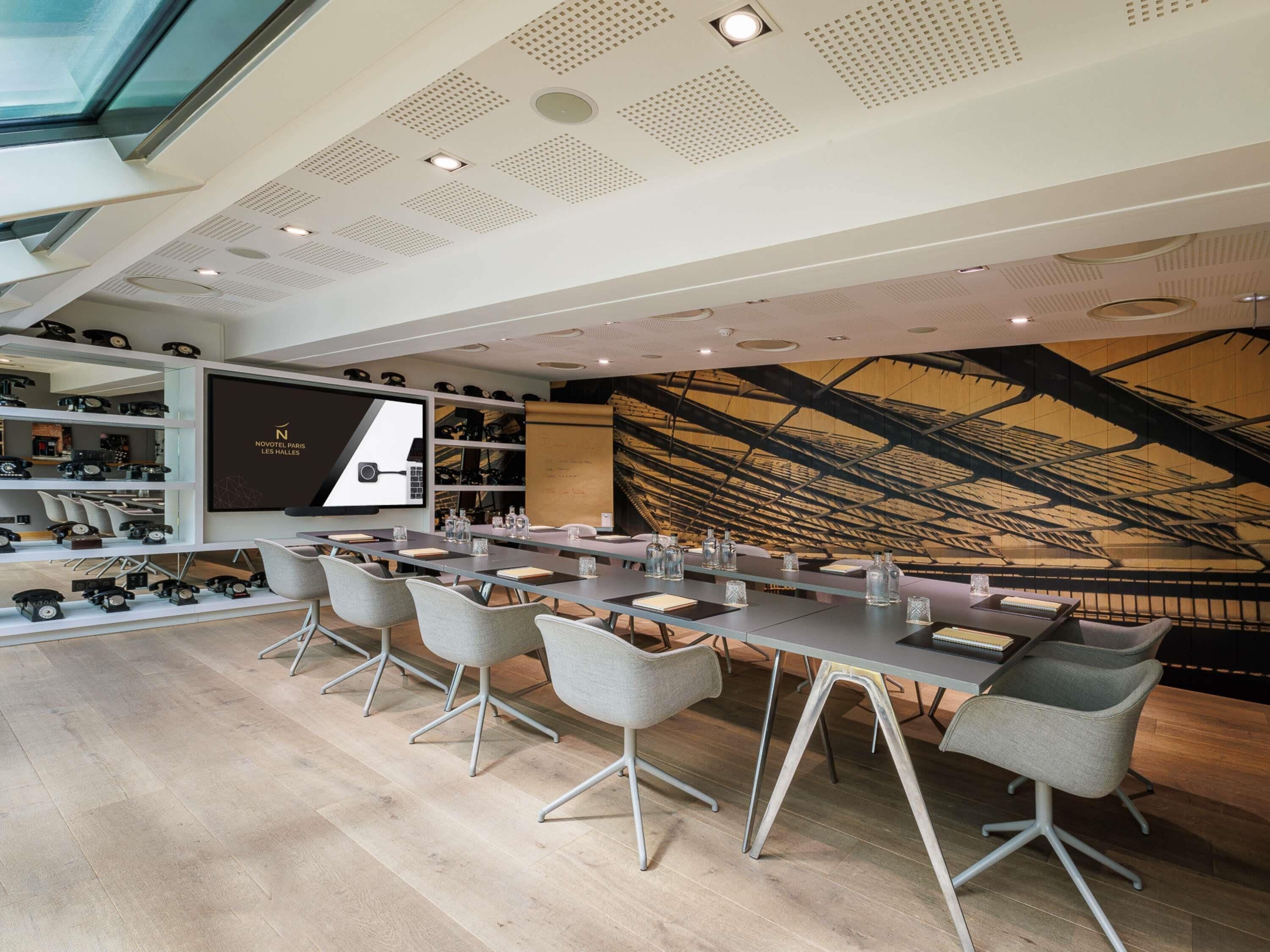 A modern conference room with a long table, grey chairs, a projector screen, and a wooden ceiling design.