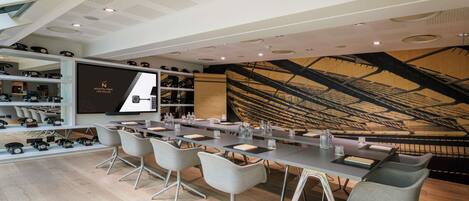 A modern conference room with a long table, grey chairs, a projector screen, and a wooden ceiling design.