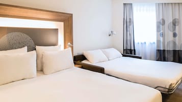 Habitación de hotel con dos camas, cabecero de madera, lámpara de pared y ventana con cortinas estampadas.