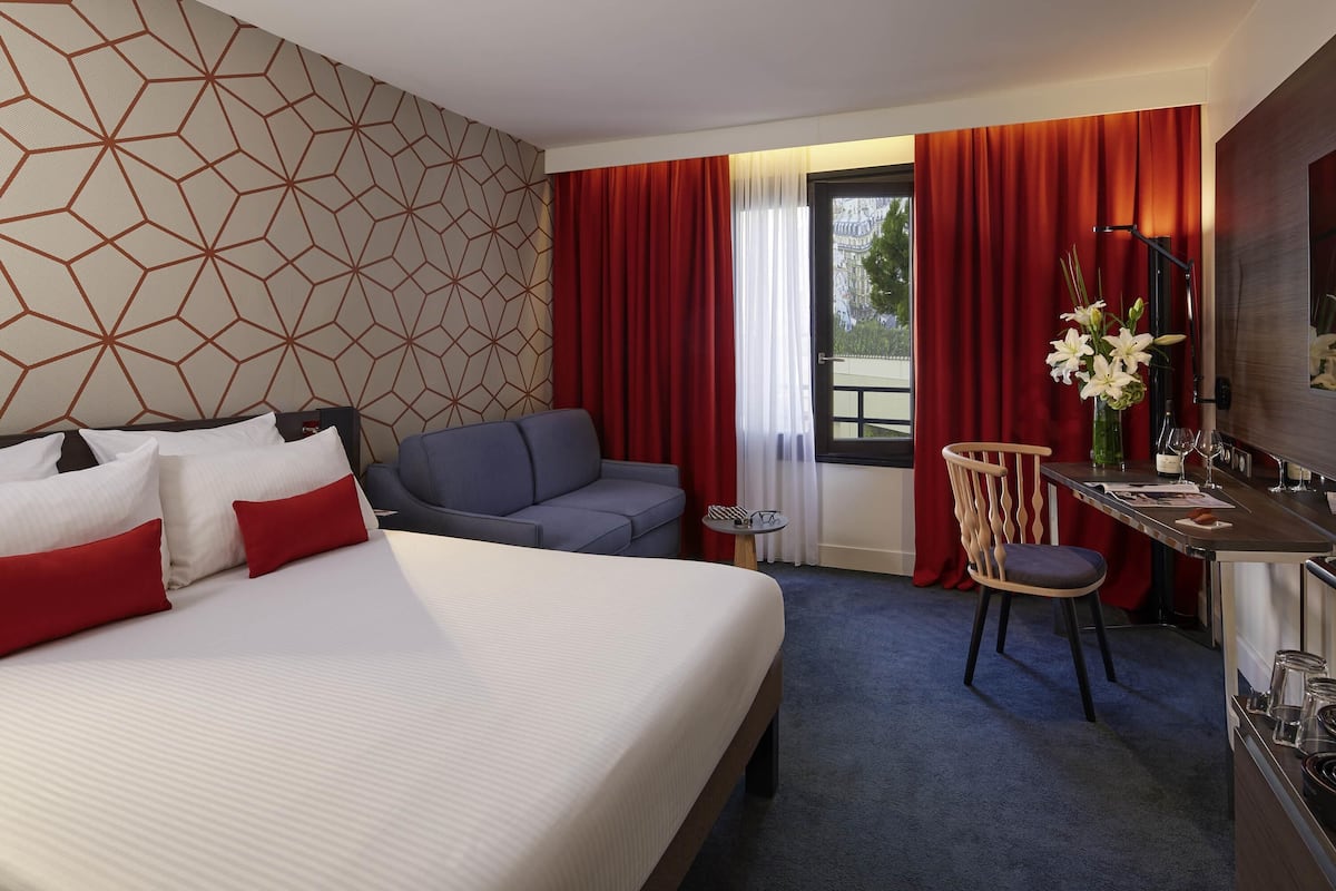 A hotel room with a bed, a sofa, a desk, and a TV.