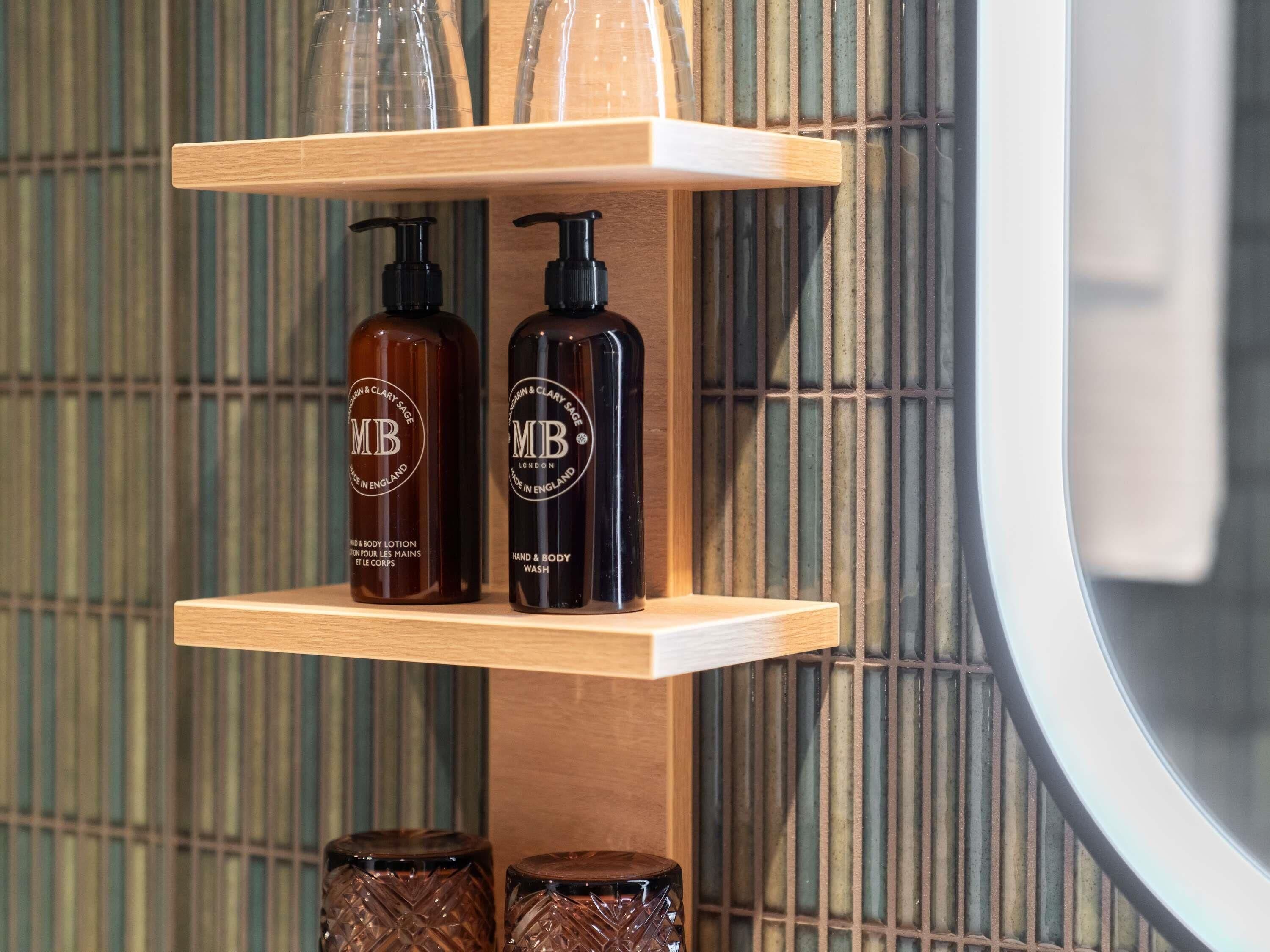 A bathroom shelf with two hand and body wash bottles and two glass containers.