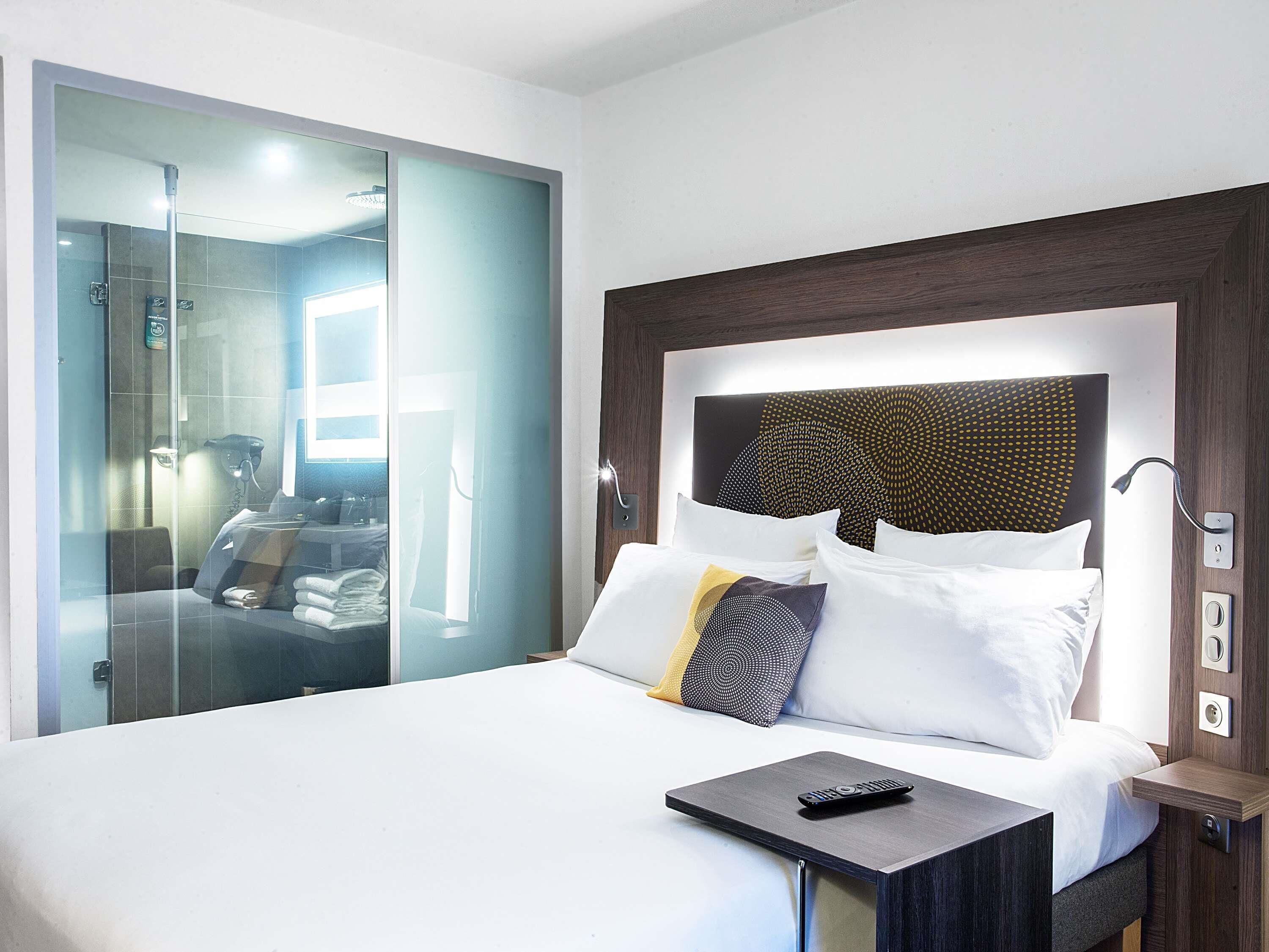 Una habitación de hotel con cama, mesita de noche y armario de vidrio.