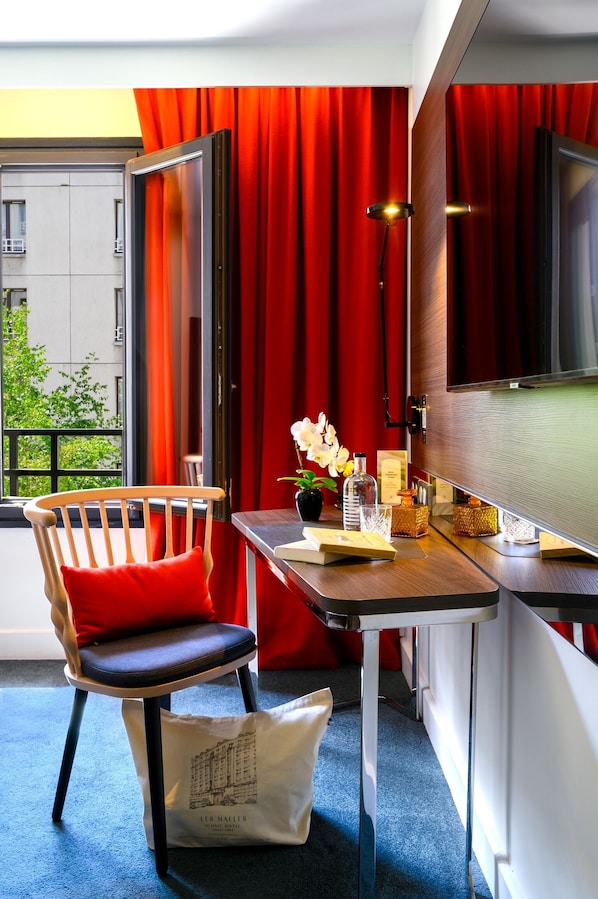 Una habitación moderna con una silla de madera, una mesita con un florero y un televisor, cortinas rojas.