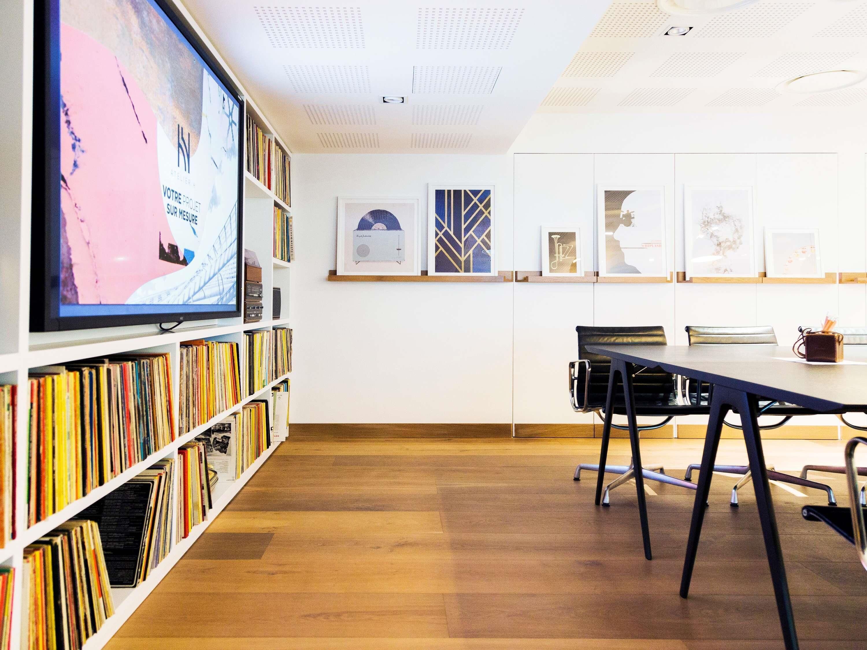 Une bibliothèque moderne, dotée d’étagères, d’un grand écran et d’œuvres d’art encadrées qui ornent les murs.