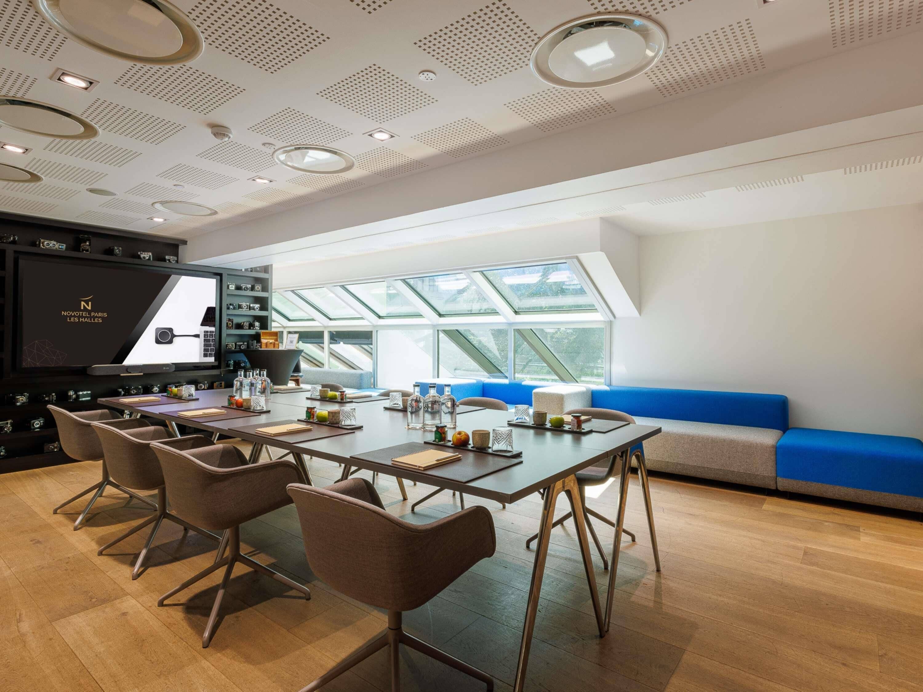 Una sala de reuniones moderna con una gran mesa, sillas, un sofá y una pantalla grande.
