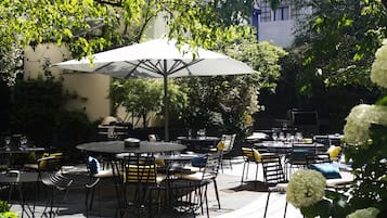 Un patio al aire libre con mesas y sillas redondas, sombrillas y una parrilla.