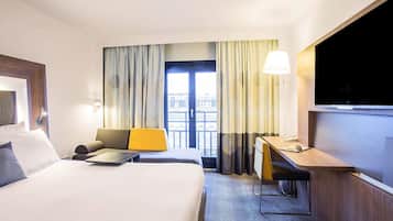 Une chambre d’hôtel avec un lit, un bureau, une chaise, une télévision et une vue sur la ville par la fenêtre.