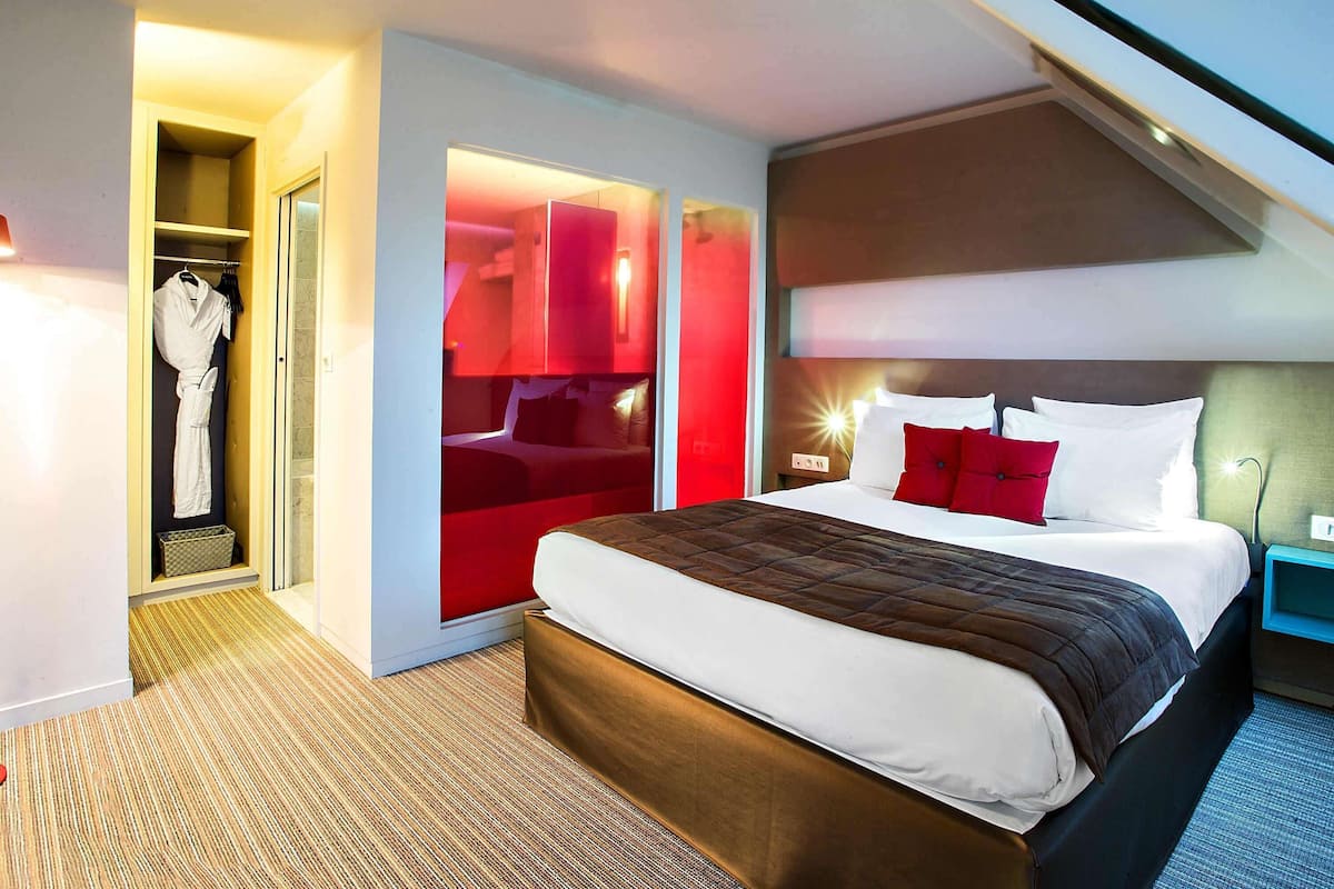 A modern hotel room with a large bed, a walk-in closet, and a red accent wall.