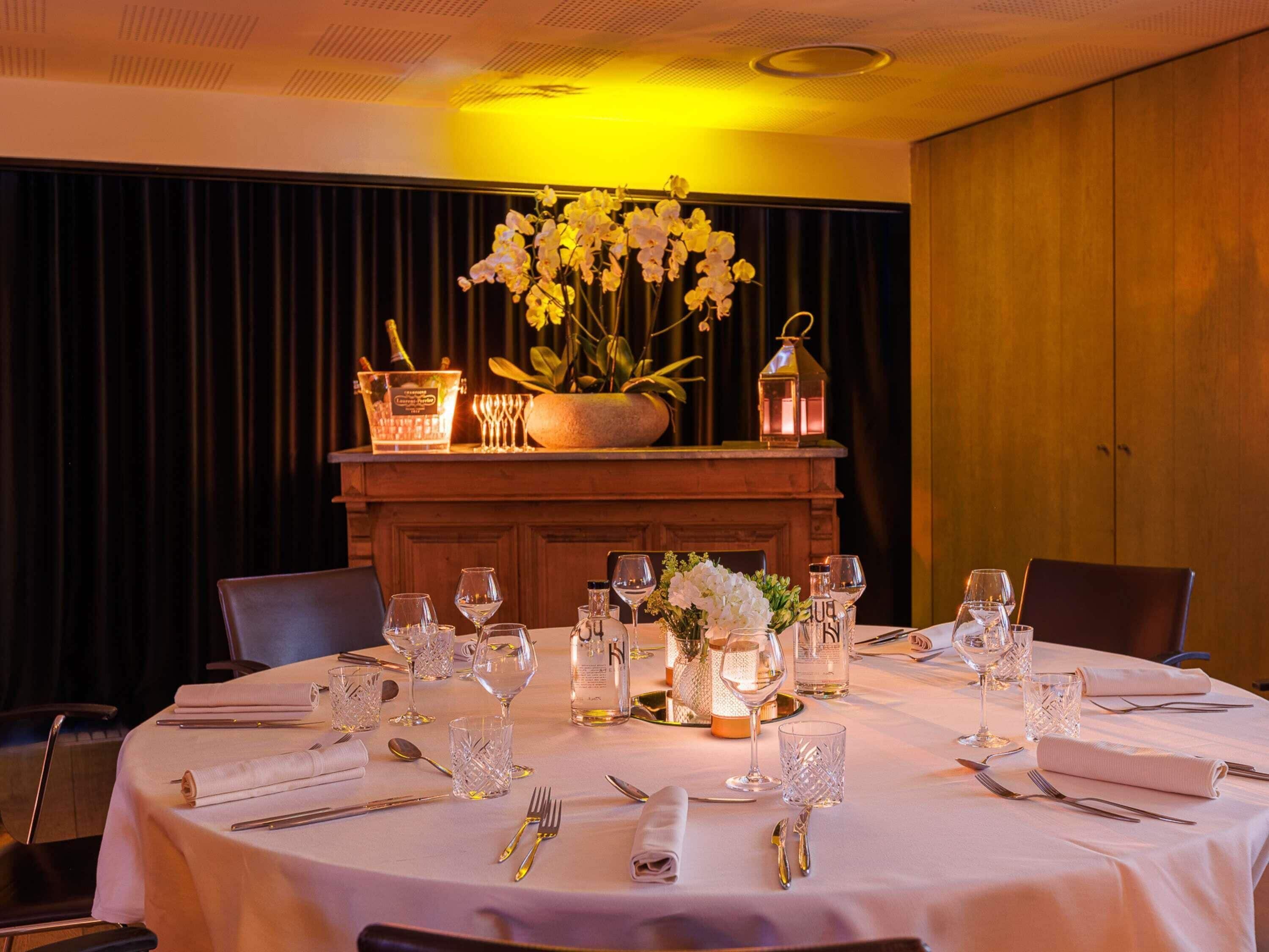 Mesa redonda dispuesta para comer, con mantel blanco, copas de vino, cubiertos y un centro de mesa con flores y un candelabro.