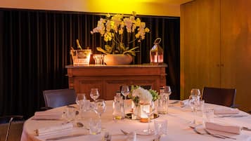 Mesa redonda dispuesta para comer, con mantel blanco, copas de vino, cubiertos y un centro de mesa con flores y un candelabro.