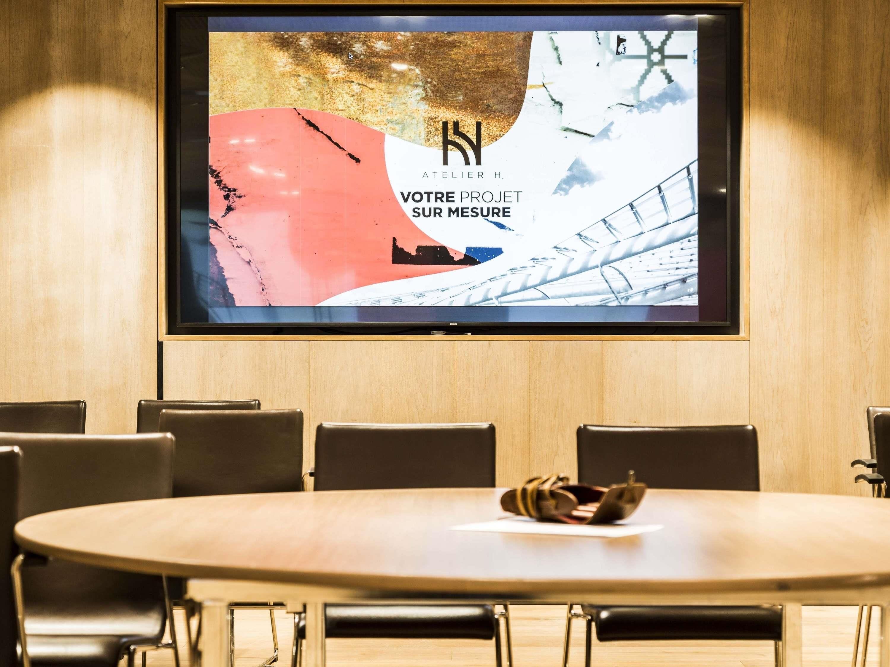 Uma sala de conferências com uma tela grande exibindo texto em francês, paredes de painel de madeira e cadeiras modernas.