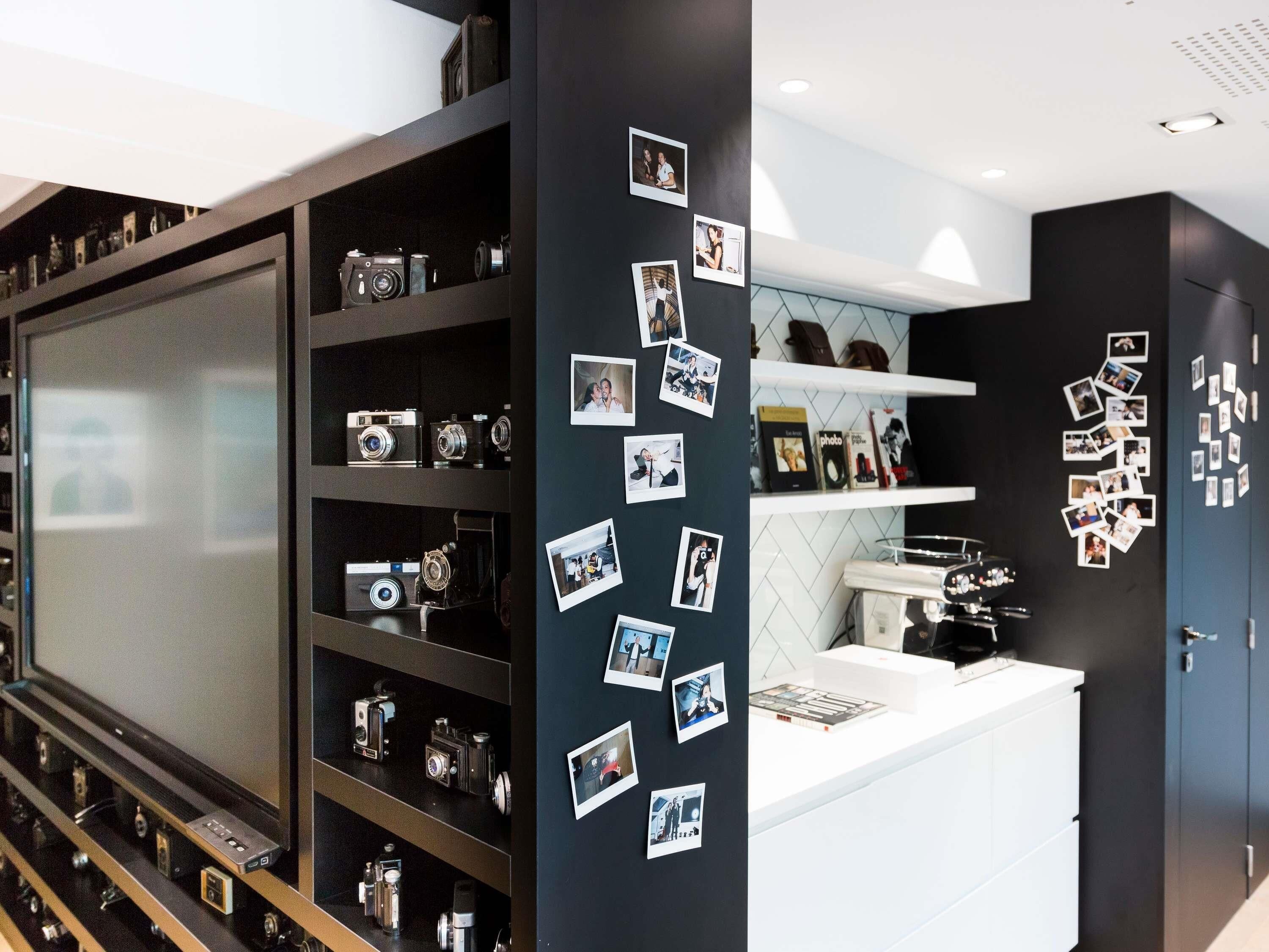 A modern room with a large screen, shelves with cameras, and a wall decorated with photos.
