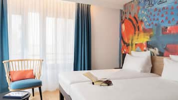 Een hotelkamer met een bed, een stoel, een tafel en een kleurrijk abstract schilderij aan de muur.