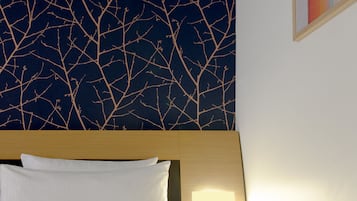 A hotel room with a bed, a nightstand, a wall-mounted light, and a wall with a tree branch pattern.