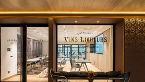Un vestíbulo de hotel con una zona de estar, un mostrador de recepción y un amplio ventanal que muestra el nombre del hotel 'VINS LIQUITS'.