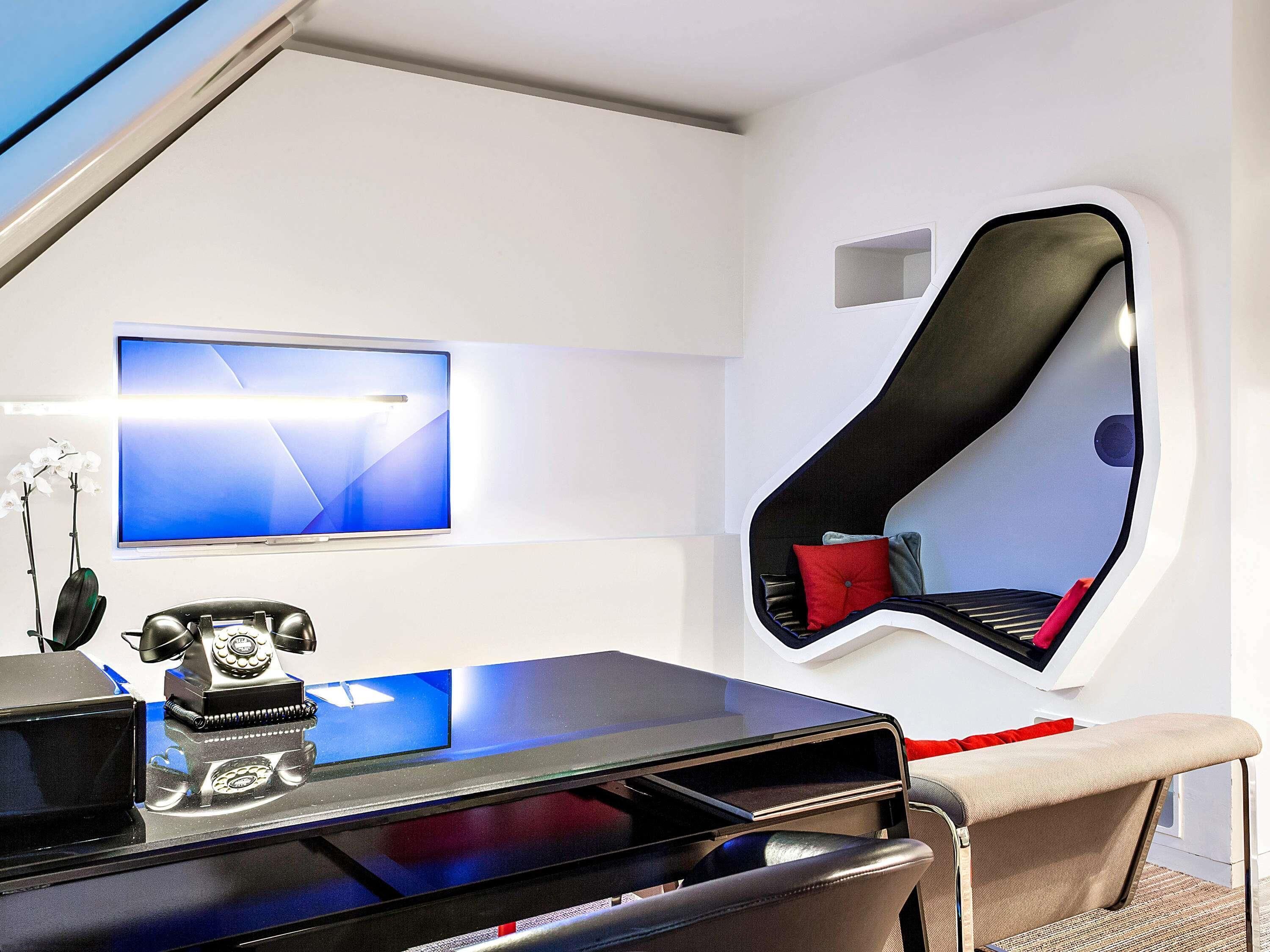 A modern room with a desk, a flat-screen TV, a vintage telephone, and a unique curved mirror.