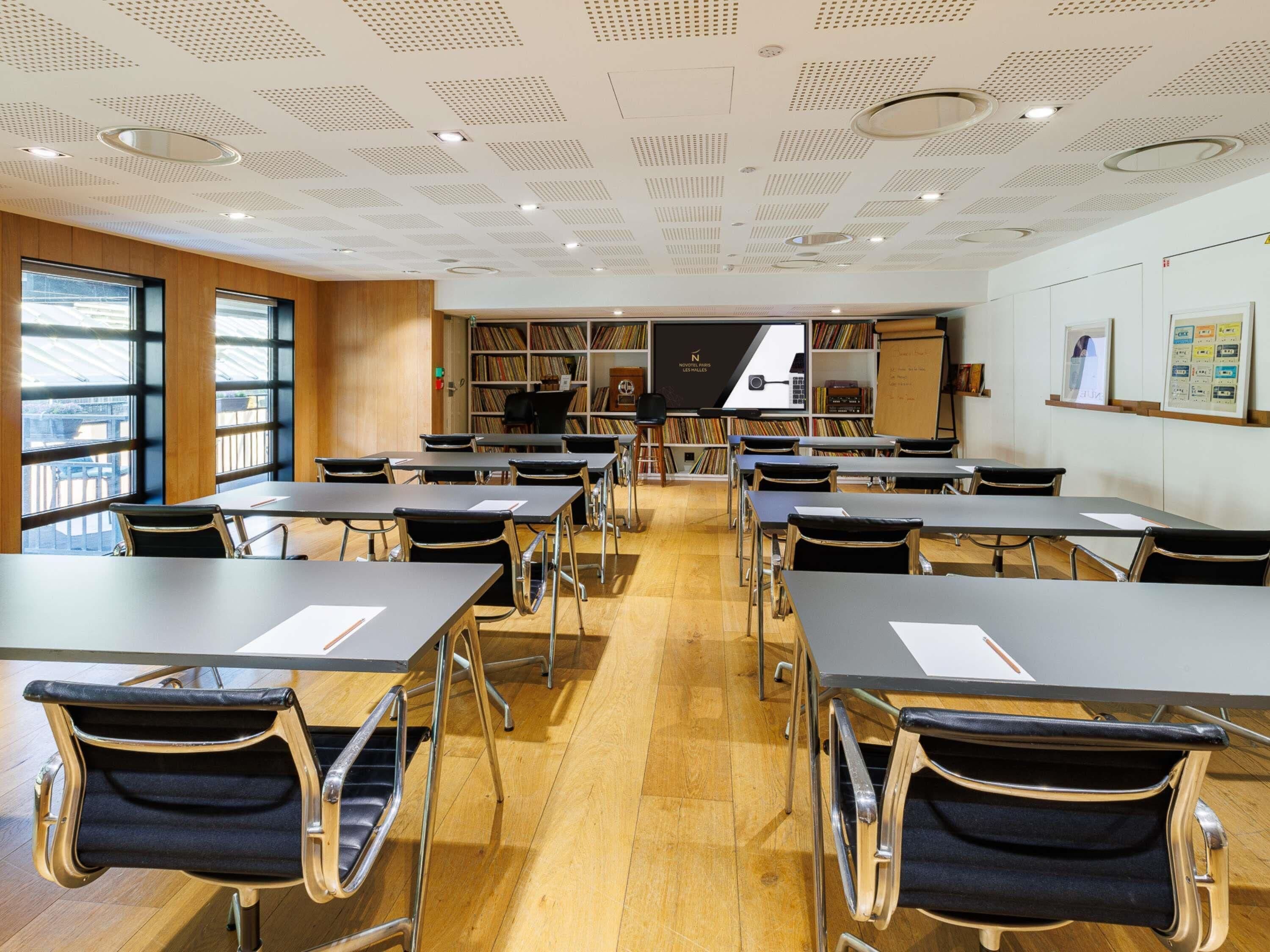 Une bibliothèque moderne, dotée de tables et de chaises, d’étagères et d’une grande fenêtre.