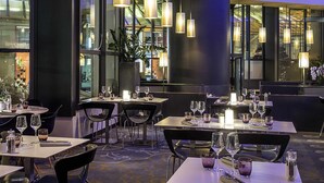 Interior de un restaurante moderno con mesas dispuestas para comer, iluminación ambiental y amplias ventanas.