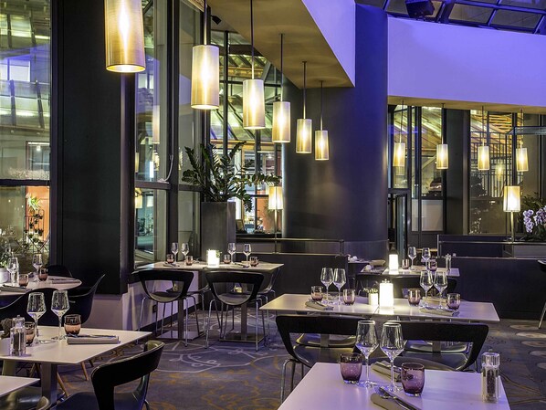 Interior de un restaurante moderno con mesas dispuestas para comer, iluminación ambiental y amplias ventanas.