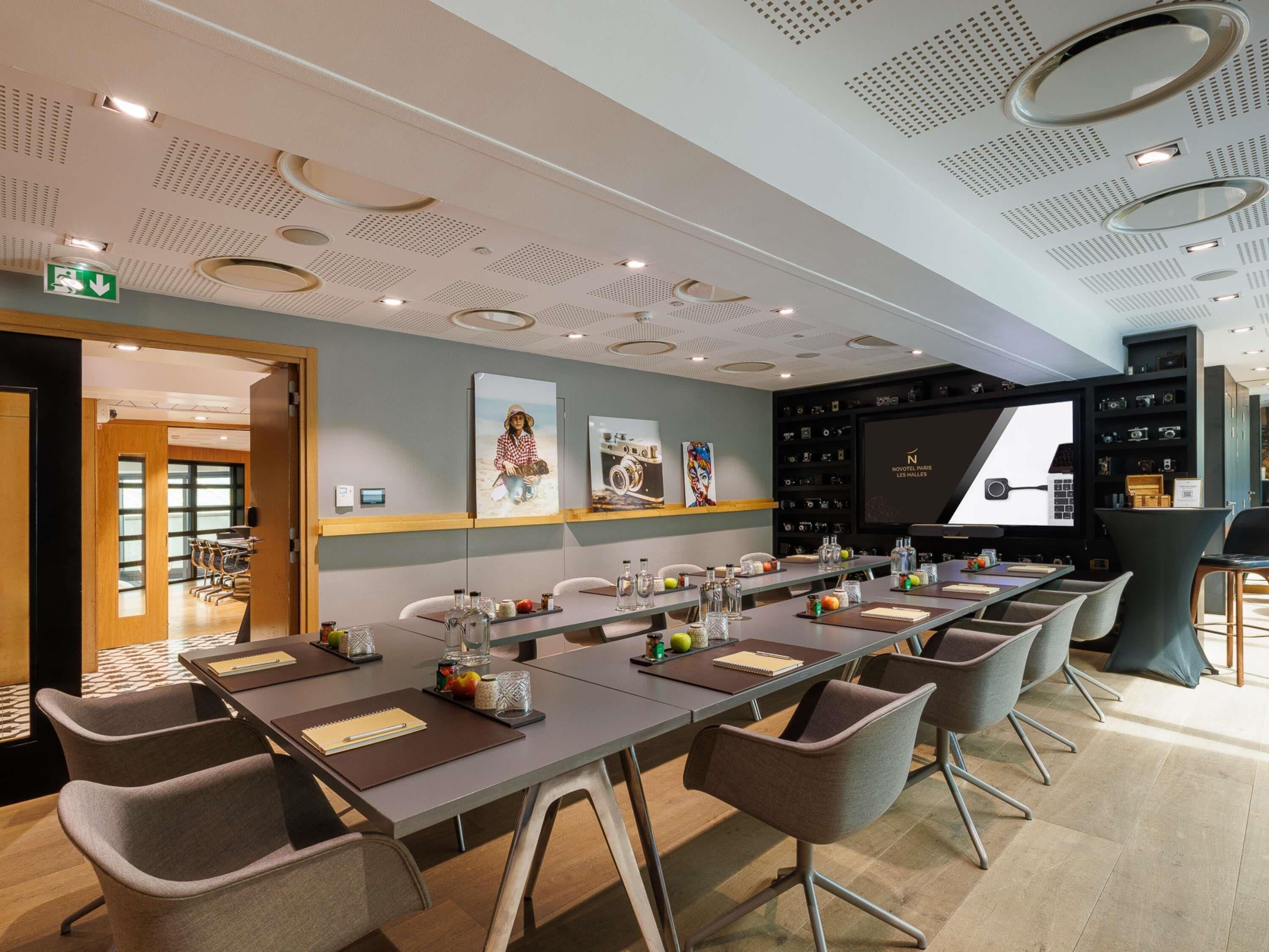 A modern conference room with a long table, chairs, a projector screen, and a wall with framed pictures.