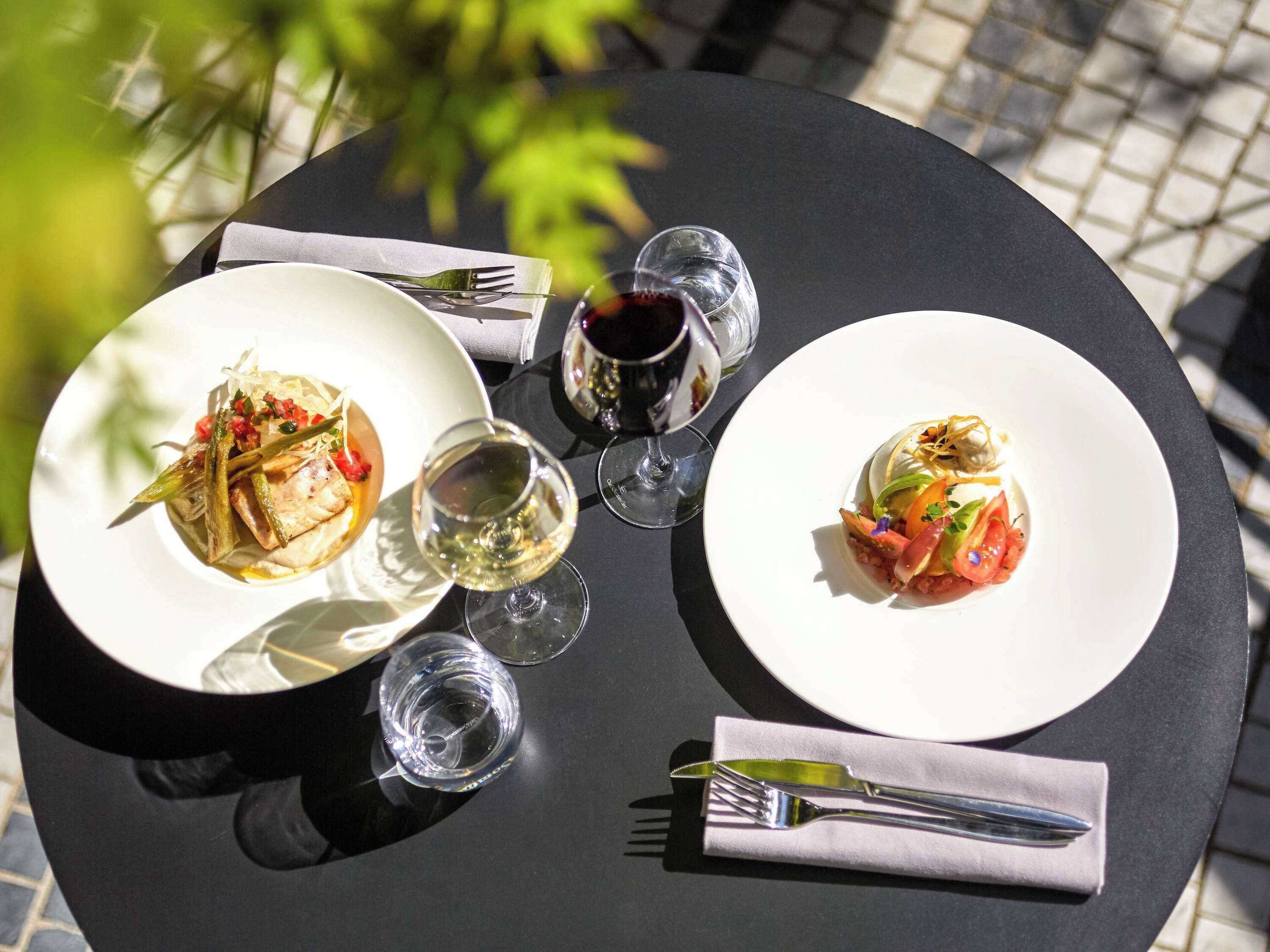 A round table with two white plates of food, two wine glasses, and cutlery.