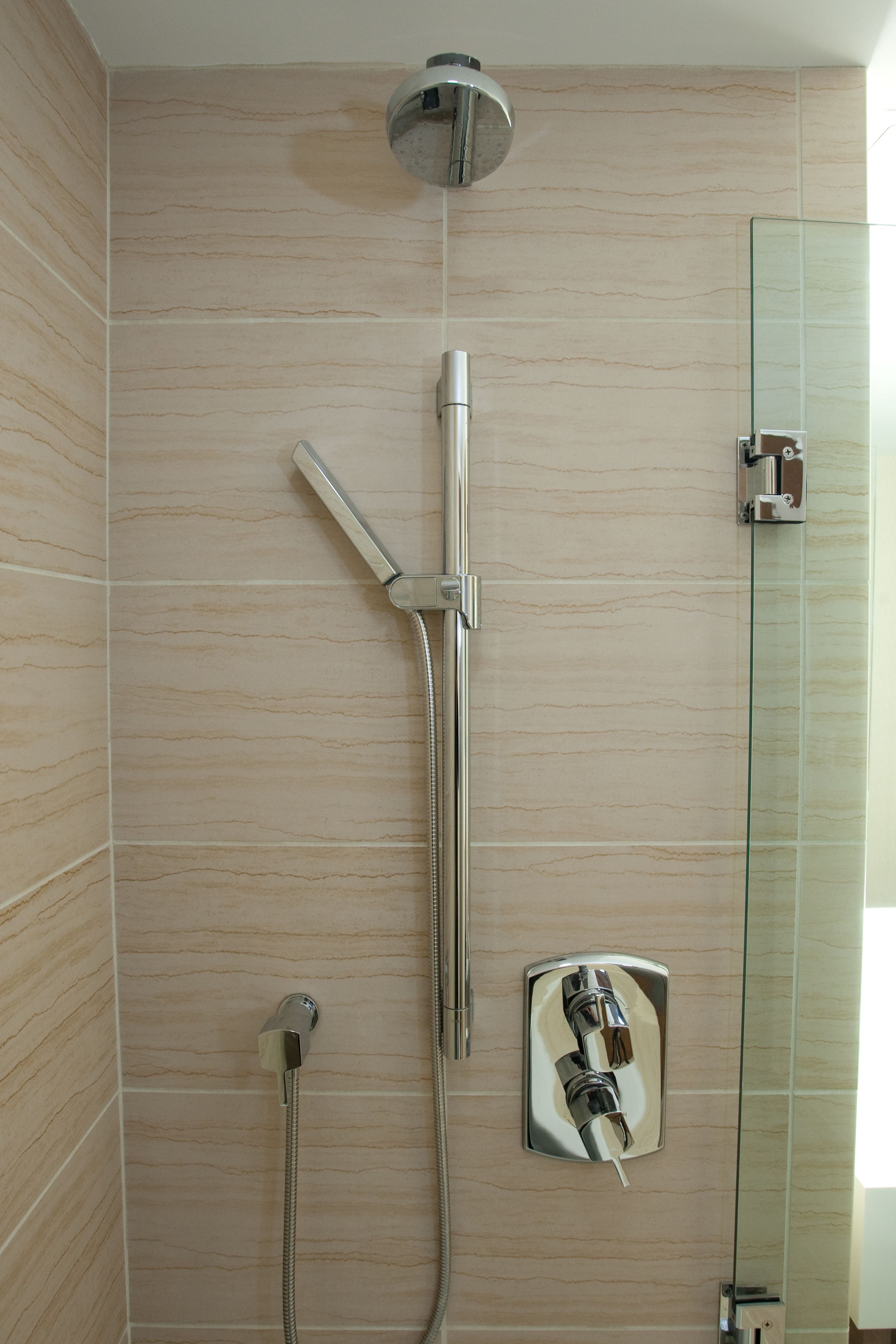 A shower with a glass enclosure, a handheld showerhead, and a wall-mounted faucet.