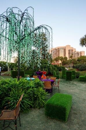 An outdoor seating area with green hedges, a table with chairs, and a decorative tree structure. - Hyatt Regency Grand Cypress (Orlando)