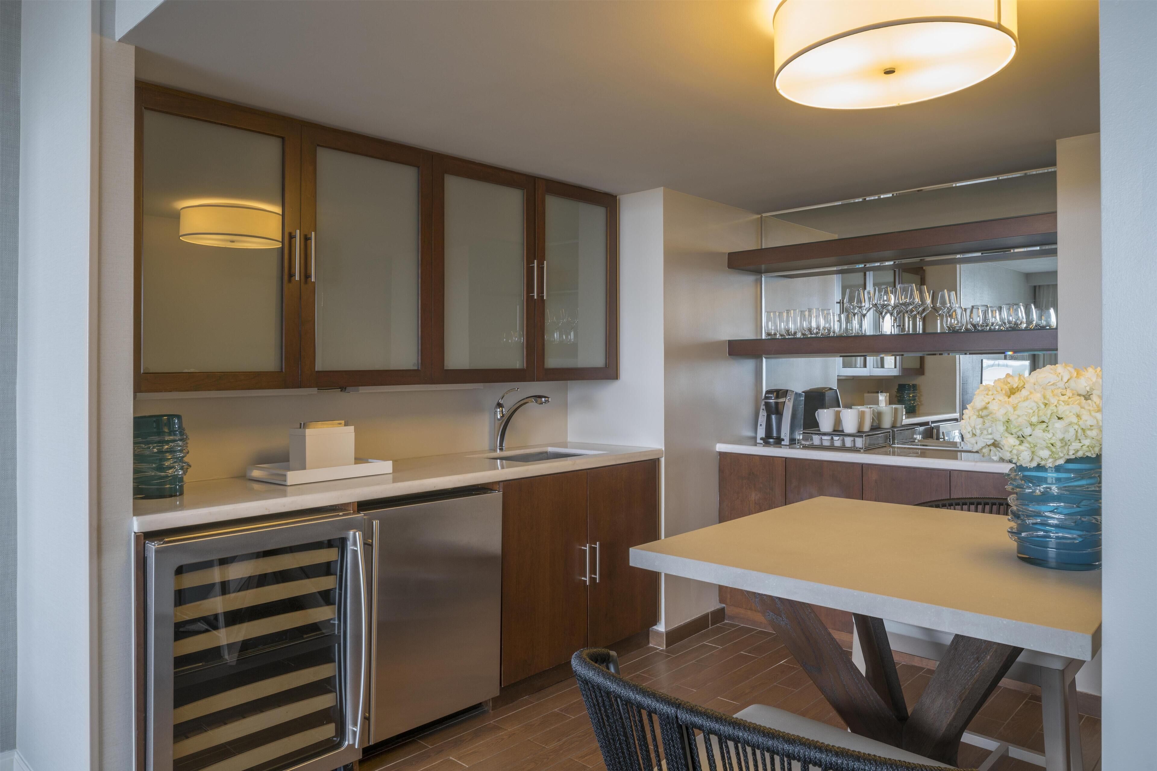 A modern kitchen with wooden cabinets, a stainless steel refrigerator, a sink, and a dining area with a table and chairs.